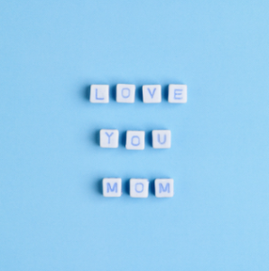 Square letter beads spelling out 'Love You Mom' against a blue background.