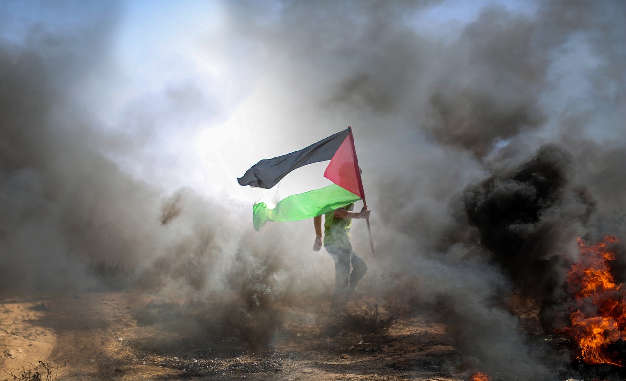 A man in Gaza carrying a Palestinian flag through smoke and fire. Image by hosny salah from Pixabay