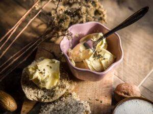 Picture of fresh butter with herb in a pink flower shaped bowl and some bread with butter to the side.